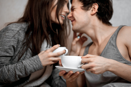 Young beautiful pair of lovers drink tea (coffee) in bedの写真素材