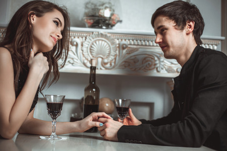 Beautiful young couple with glasses of red wine in luxury restaurantの写真素材