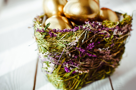 Golden easter eggs in nest on white wooden backgroundの写真素材