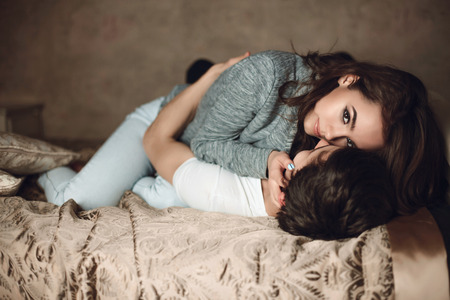 beautiful brunette girl lies on top on guy on the bedの写真素材