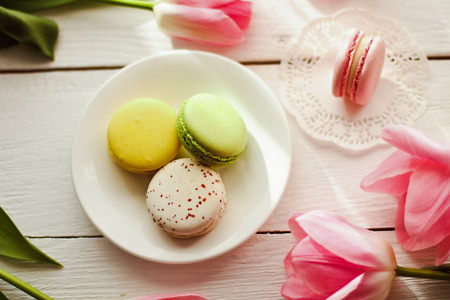 A beautiful flowers pink tulips with colorful macaroons laid on a white platter on white wooden backgroundの写真素材