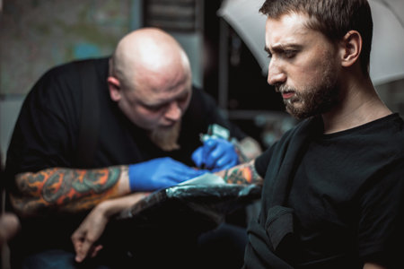 master tattoo artist with a beard makes gloves tattoo on hand menの写真素材