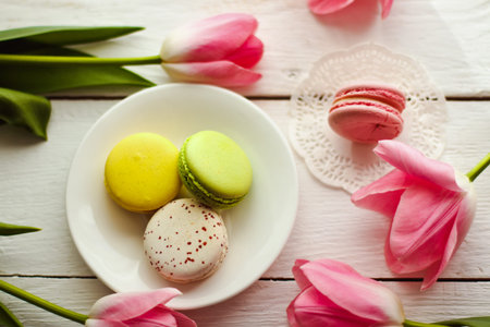 A beautiful flowers pink tulips with colorful macaroons laid on a white platter on white wooden backgroundの写真素材