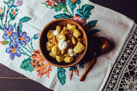 Beautiful hot dumplings with sour cream and fried onions in a clay bowl with a wooden spoon are embroidered on the towelの写真素材