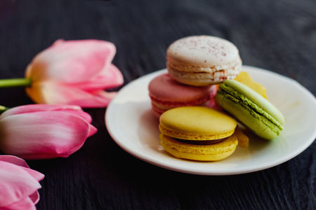 A beautiful flowers pink tulips with colorful macaroons laid on dark wooden backgroundの写真素材