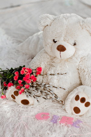 A beautiful soft toy bear sits on the bed with flowersの写真素材