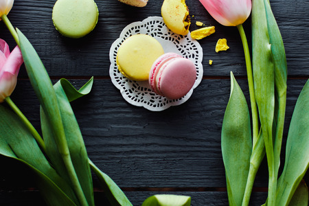 A beautiful flowers pink tulips with colorful macaroons laid on dark wooden background with Lacy napkinの写真素材