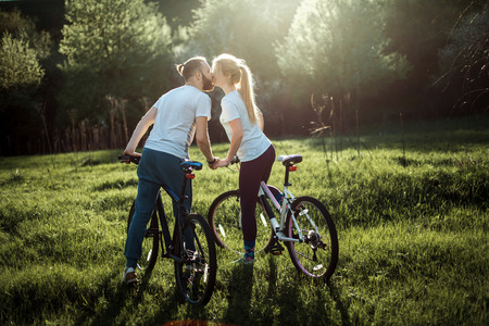 Beautiful young couple in love walking with bicycles, kissing and hugging.の写真素材