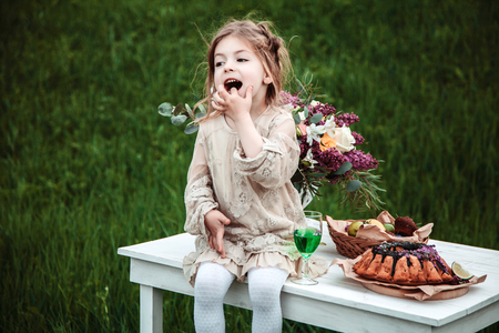 Little baby girl eats chocolate cake in nature at a picnic.の写真素材