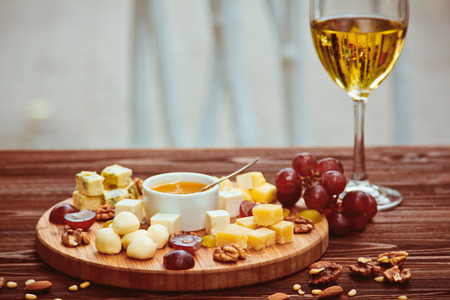 Cheese Board served with grapes, nuts and a glass of white wine on a wooden backgroundの写真素材