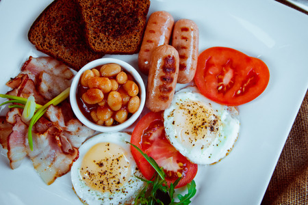Traditional Full English Breakfast - sunny-side-up fried eggs, sausages, beans, toast and baconの写真素材