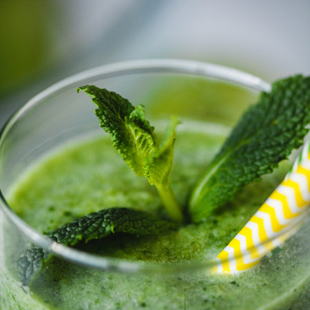 Healthy green smoothie from apples, spinach and kiwi with mint in a glass with a straw on wooden...