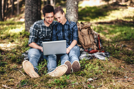 A couple of tourists sitting and looking at laptop in the woods.の写真素材