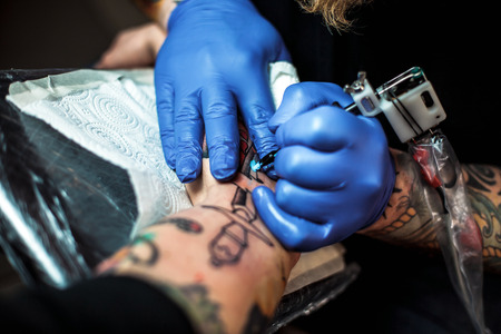 master tattooist makes a tattoo on the skin of the client in a workshop with special equipmentの写真素材