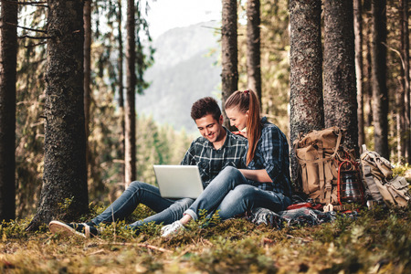 A couple of tourists sitting and looking at laptop in the woods. The concept of active restの写真素材