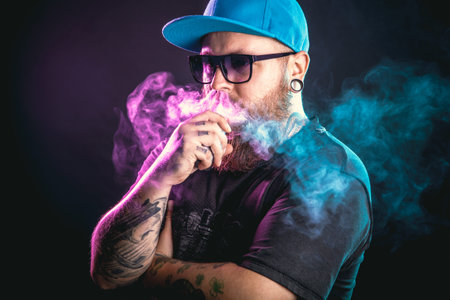 Men with beard  in sunglasses vaping and releases a cloud of vapor.