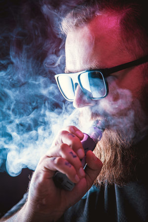 Men with beard  in sunglasses vaping and releases a cloud of vapor.