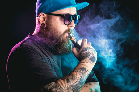Men with beard  in sunglasses vaping and releases a cloud of vapor.の写真素材
