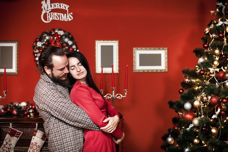 Family portrait in home holiday living room, loving young couple hugging near the Christmas tree in decorated New Year interiorの写真素材