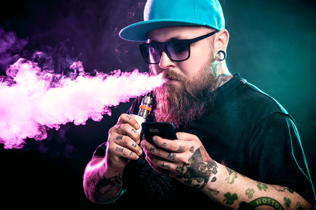 Men with beard  in sunglasses vaping and releases a cloud of vapor.の写真素材