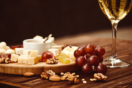 Cheese Board served with grapes, nuts and a glass of white wine on a wooden backgroundの写真素材