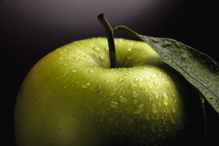 Large beautiful green apple with a leaf and water drops on a dark backgroundの写真素材