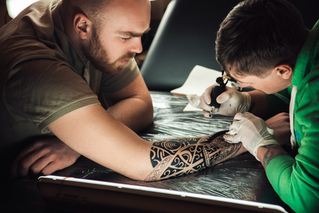 Master tattoo artist in gloves makes tattoo on hand menの写真素材
