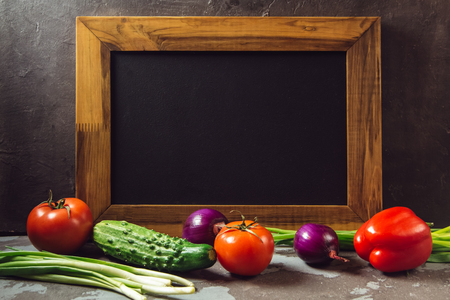 Fresh vegetables on the table are tomatoes, cucumbers, green onions on the background of an empty frameの写真素材