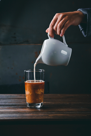 Close-up of barista girl hands, preparing proper cappuccino pouring Milk into a glass of coffee. Concept of tasty aroma coffeeの写真素材