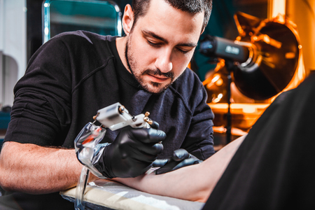 master tattooist makes a tattoo on the skin of the hand client girl in a workshop with special equipmentの写真素材
