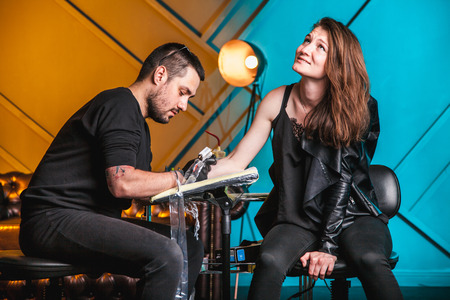 master tattooist makes a tattoo on the skin of the hand client girl in a workshop with special equipmentの写真素材