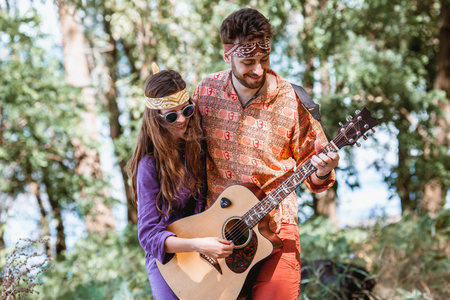 Beautiful young couple in love in hippie style with the guitar resting on the beach in summer. A Girl holding a guitar, man teaches how to play his girlfriend on the seafrontの写真素材