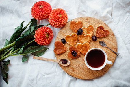 A homemade Breakfast or late Breakfast: American pancakes in the shape of a heart style, served with berries, blackberries and a Cup of black tea with a bouquet of flowersの写真素材