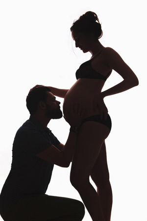 A beautiful pregnant woman in lingerie, the husband kneels and strokes his belly with a future child. Couple in love, family life, values, childrenの写真素材