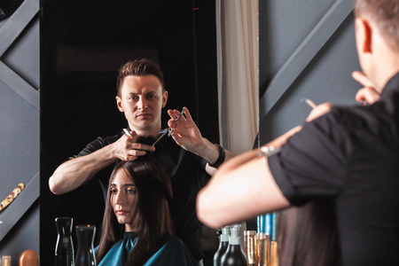 Hairdresser cutting hair, does a hairstyle of girl client. Hairstylist serving client at barber shop.の写真素材