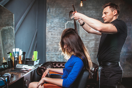 Hairdresser cutting hair, does a hairstyle of girl client. Hairstylist serving client at barber shop.の写真素材