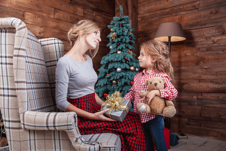 Beautiful happy mother with her daughter hold the gift in New Year interior with Christmas tree. The concept of a family celebration, a Christmas storyの写真素材