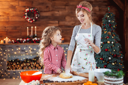 Merry Christmas and Happy Holidays. Family preparation holiday food. Mother and daughter cooking cookies in New Year interior with Christmas tree.の写真素材
