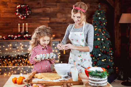 Merry Christmas and Happy Holidays. Family preparation holiday food. Mother and daughter cooking cookies in New Year interior with Christmas tree.の写真素材