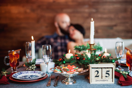 Beautiful young couple behind the decorated Christmas dinner table at the decorated New Year interior with tree. Christmas eve, calendar date of 25 on the tableの写真素材