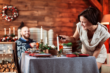 Beautiful young couple cover the table in preparation for Christmas dinner in the beautifully decorated New Year interior with Christmas treeの写真素材