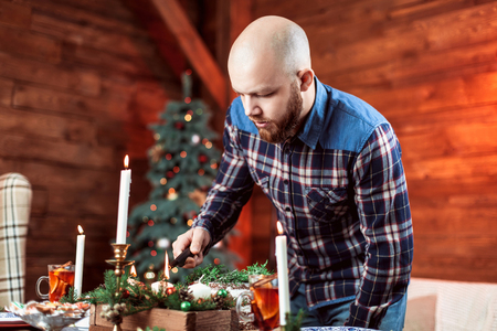 A man with a beard in the process of preparing the Christmas table. The concept of a family celebration, gala dinnerの写真素材
