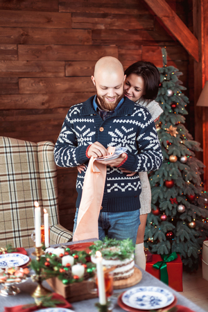 Beautiful young couple hugging and laughing behind the decorated Christmas dinner table at the nicely decorated New Year interior with Christmas treeの写真素材