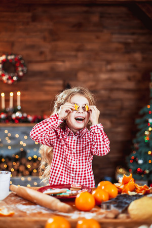 Happy little child, cute kid girl at the table in domestic kitchen making gingerbread xmas cookies decorated for Christmas holiday. Girl helping and having funの写真素材