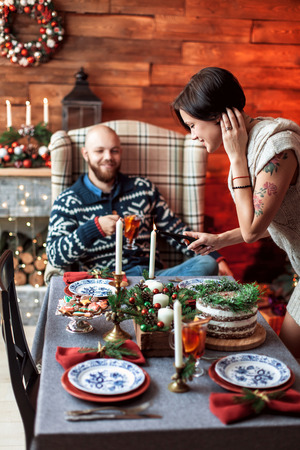 Beautiful young couple cover the table in preparation for Christmas dinner in the beautifully decorated New Year interior with Christmas treeの写真素材