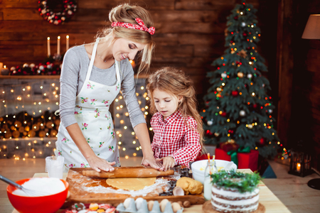 Merry Christmas and Happy Holidays. Family preparation holiday food. Mother and daughter cooking cookies in New Year interior with Christmas tree.の写真素材