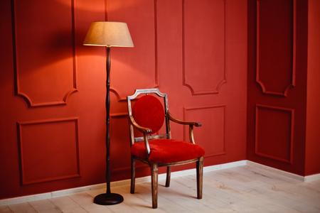 A beautiful luxurious interior of the room with an armchair and a glowing lamp against a red wall. Christmasの写真素材