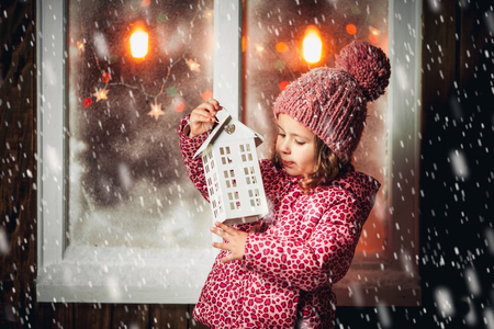On Christmas night an adorable little  girl laugh with Christmas lantern in hand near the window the snow falls.の写真素材