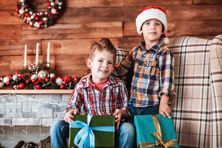 Beautiful happy laughing children brothers  play with gifts in hand in a Christmas interior with a Christmas tree. The concept of a family holidayの写真素材