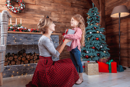 Beautiful happy mother with her daughter open a gift in New Year interior with Christmas treeの写真素材